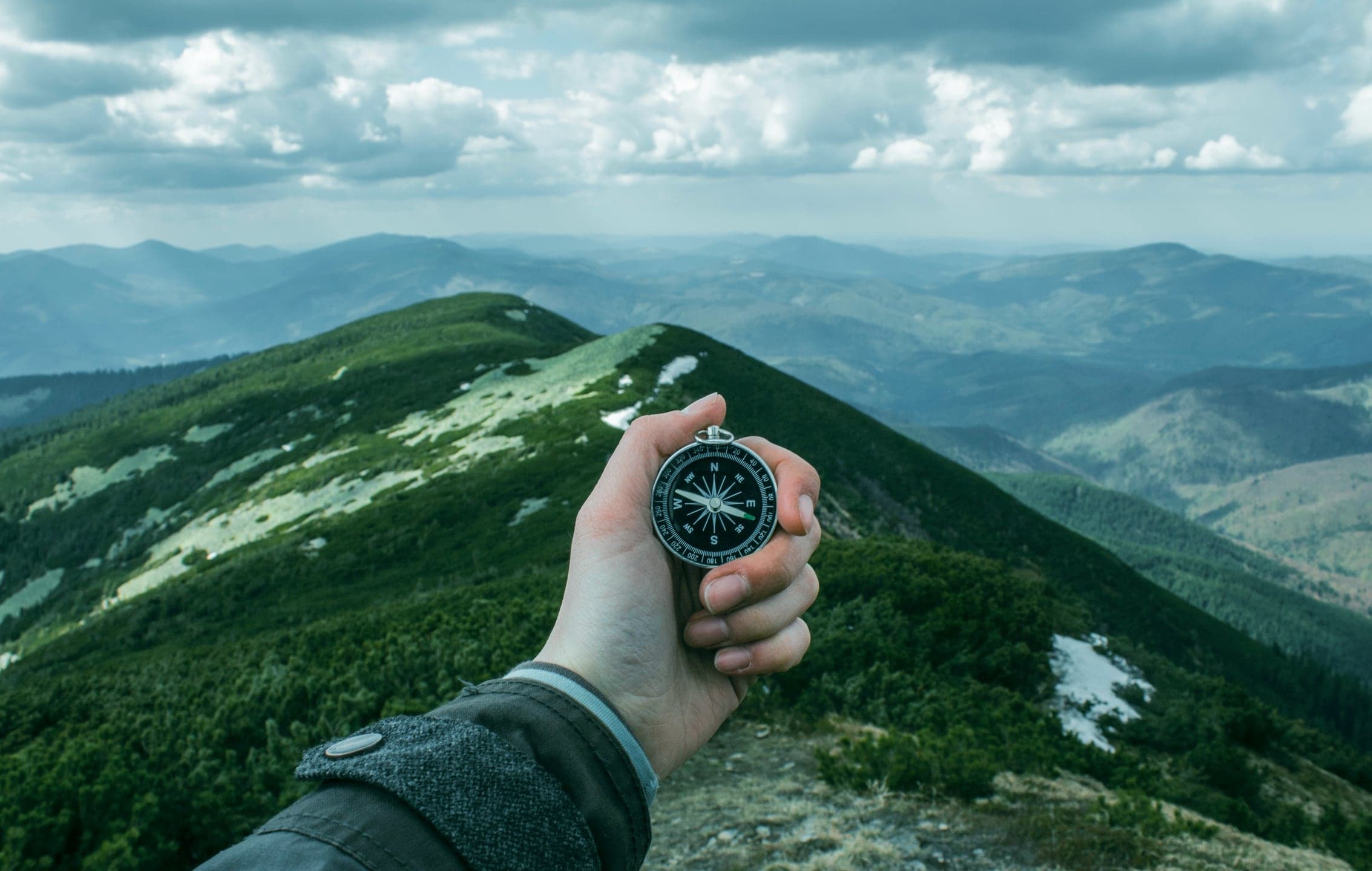 A hand holding a compass over a green mountain ridge