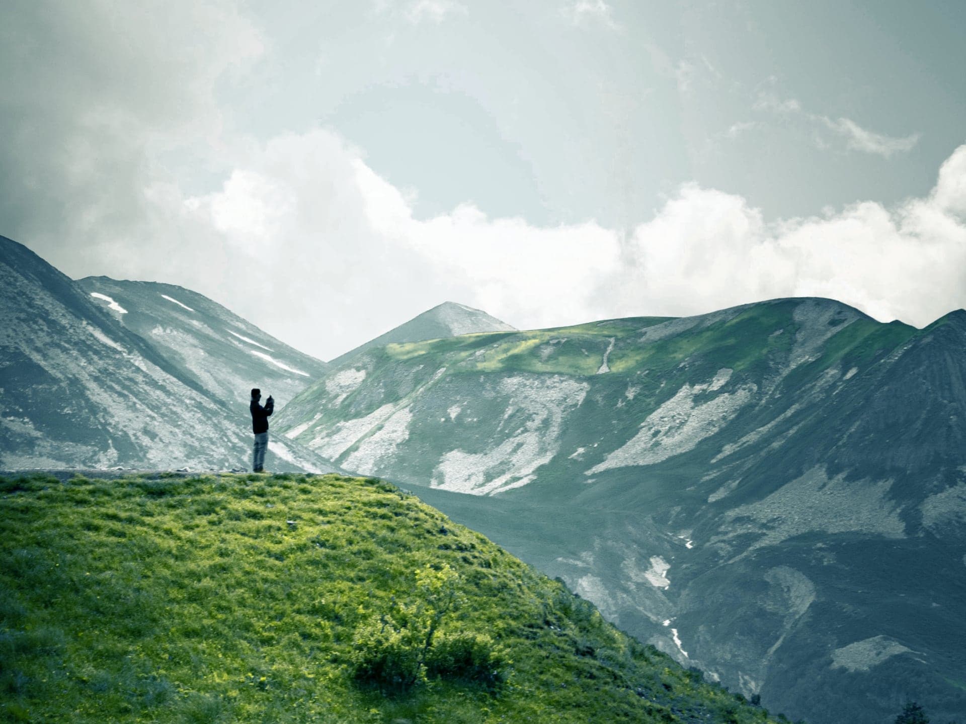 A hiker standing on a green ridge looking out over misty mountains